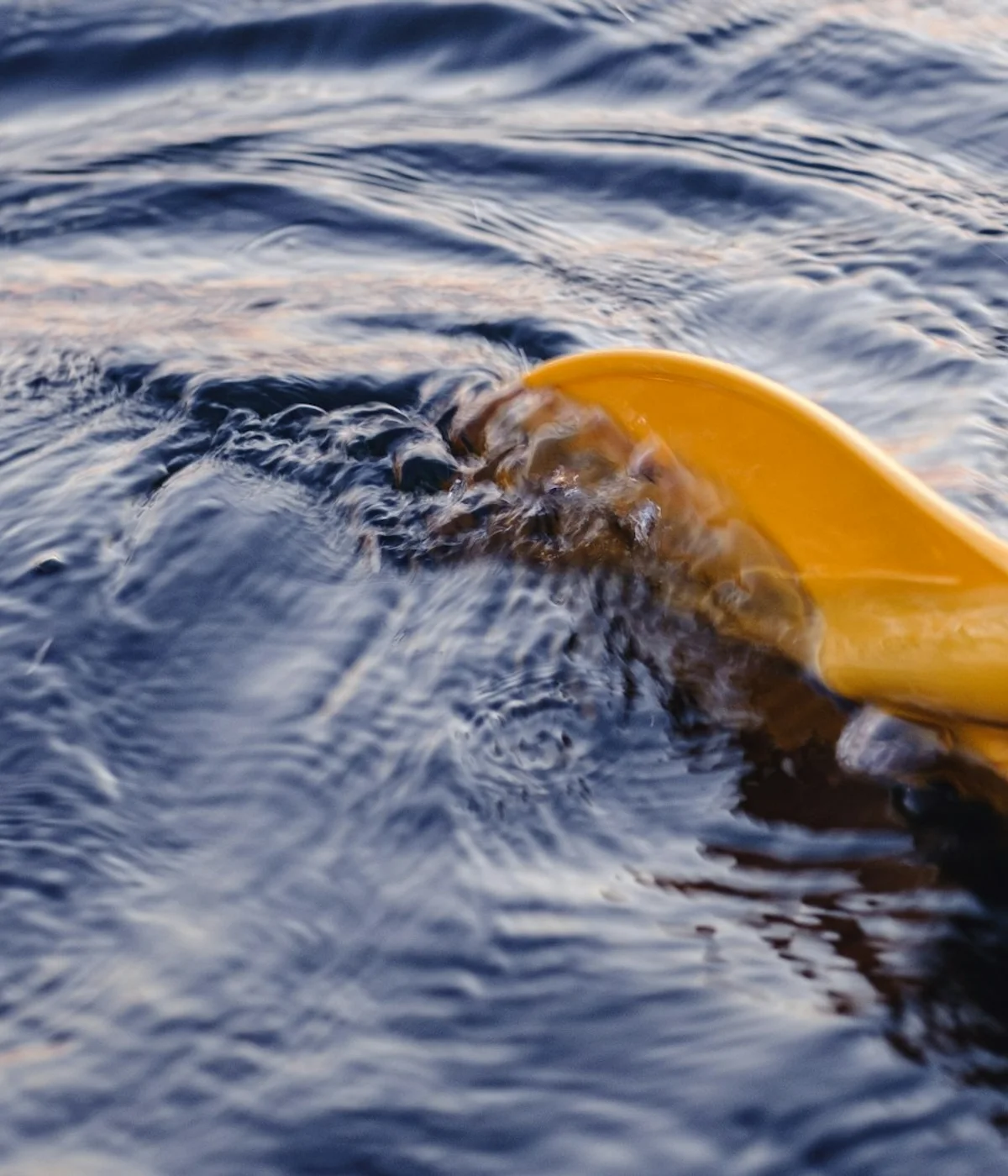 Yellow kayak paddle blade entering moving water