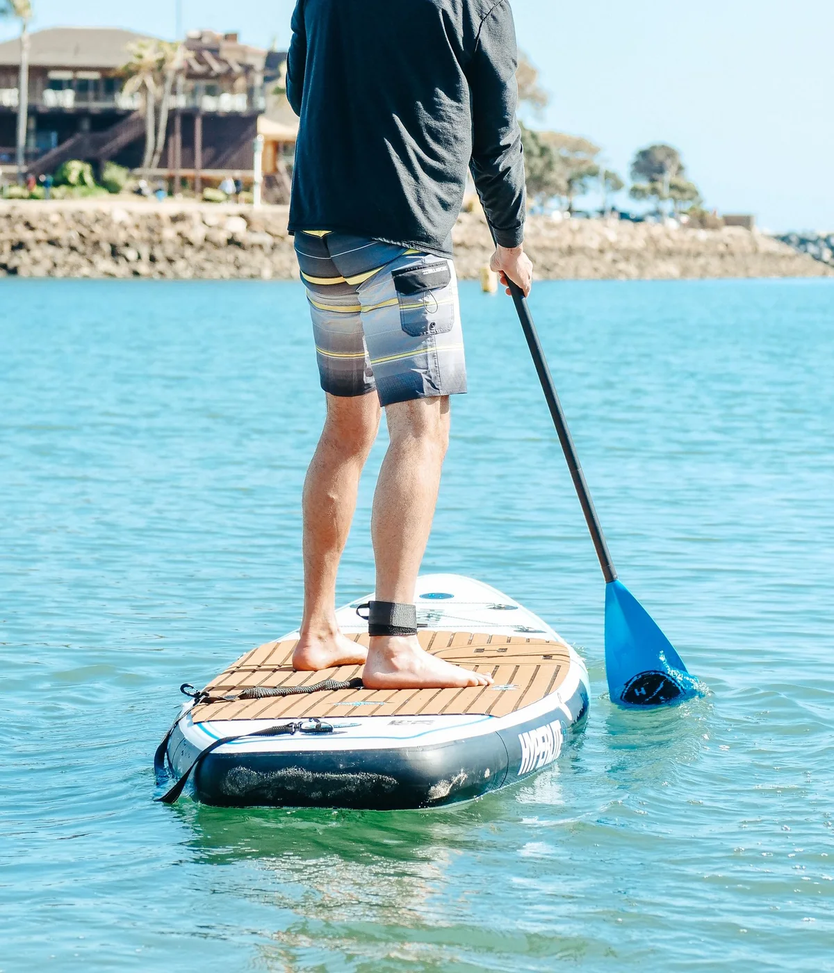 Paddler using a blue-bladed SUP paddle on calm coastal water